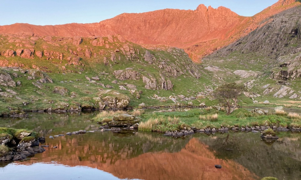 Crib Goch, an impressive rocky ridge, at sunrise with reflections in a pool of water.